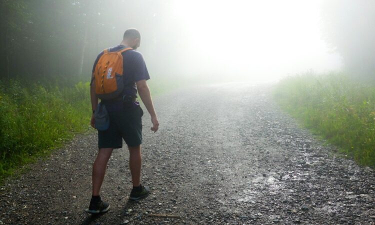 a man with a backpack walking down a foggy road